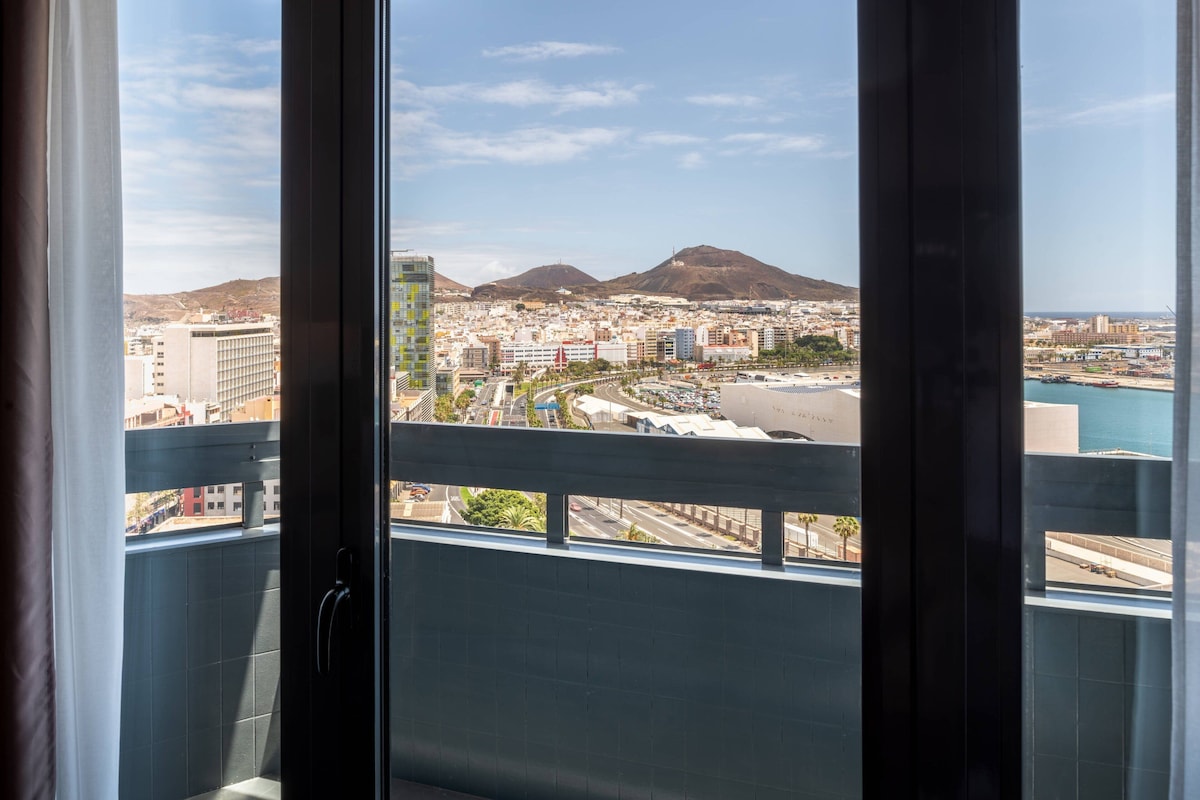 A cityscape with a mountain in the background, viewed from a balcony with a metal railing.
