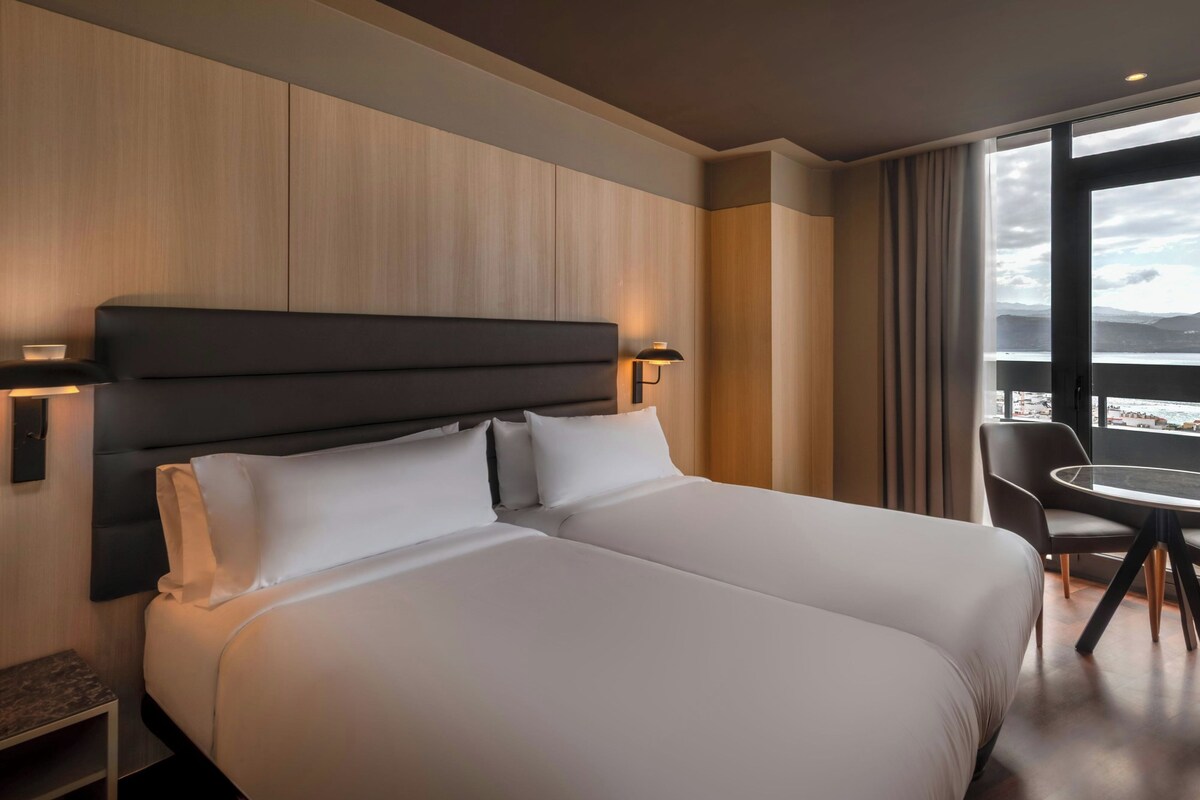 A hotel room with a large bed, a desk, and a view of the city.