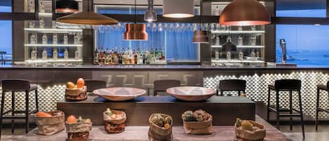 Eine moderne Bar mit einer langen Theke, verschiedenen Flaschen sowie Körben mit Brot und Früchten.
