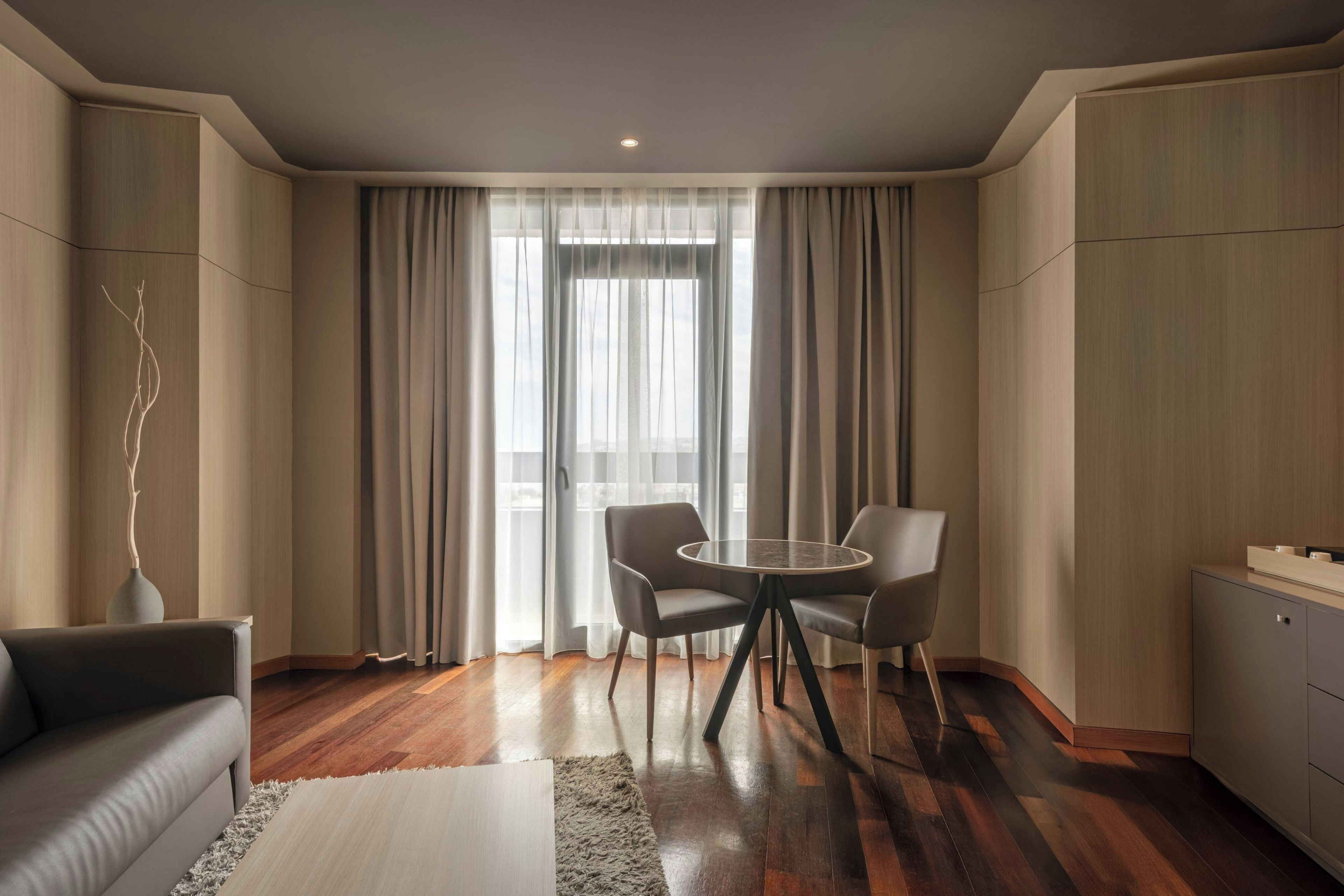 Ein modernes Zimmer mit einem runden Glastisch, zwei Stühlen, einem Sofa und einem Schrank.