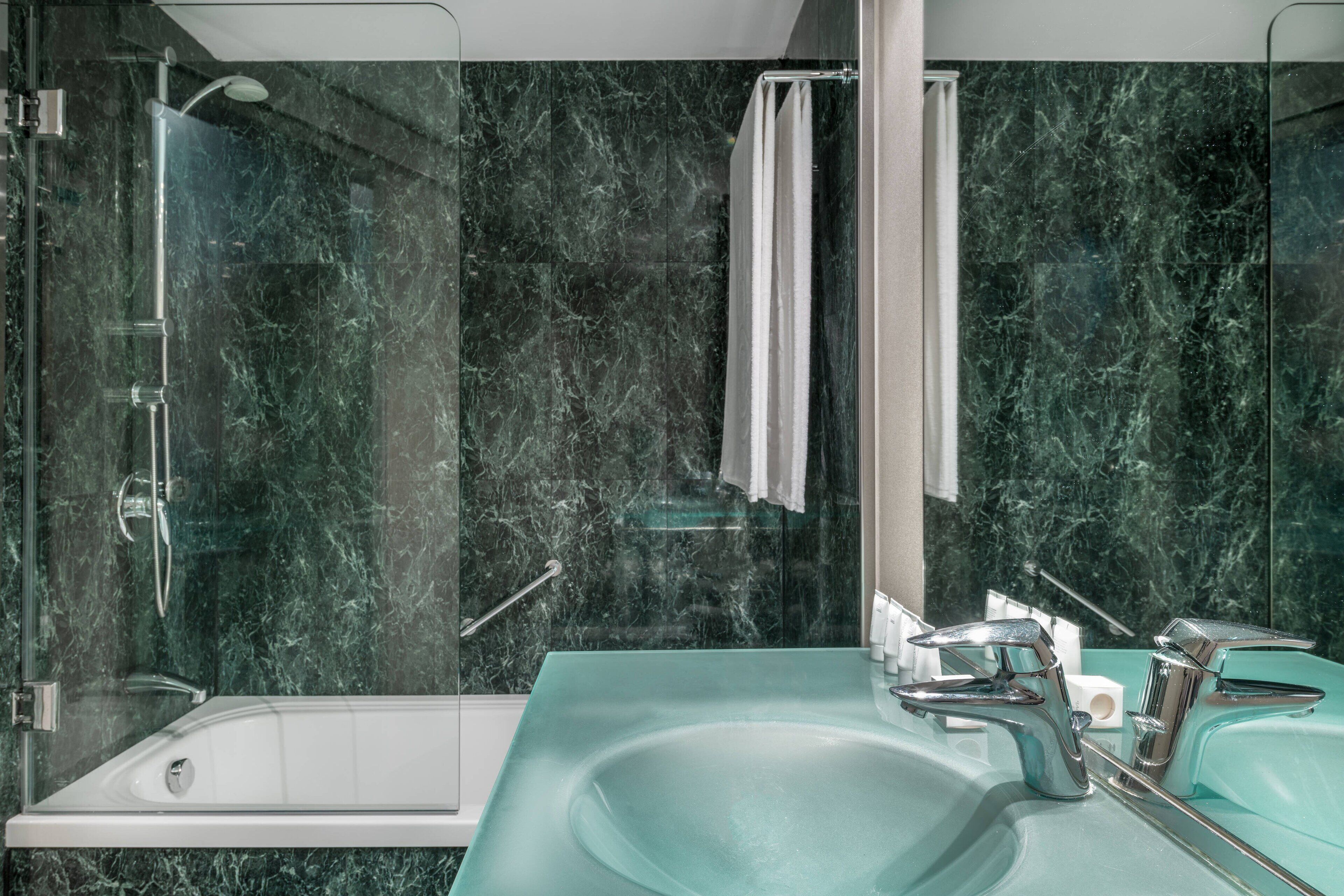 A modern bathroom with a glass-enclosed shower, a white bathtub, and a glass sink with chrome fixtures.