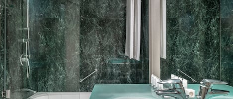 A modern bathroom with a glass-enclosed shower, a white bathtub, and a glass sink with chrome fixtures.