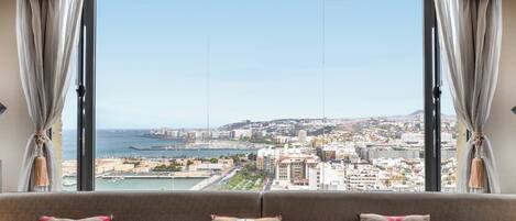 A room with a large window offering a city view, a sofa with cushions, and a table.