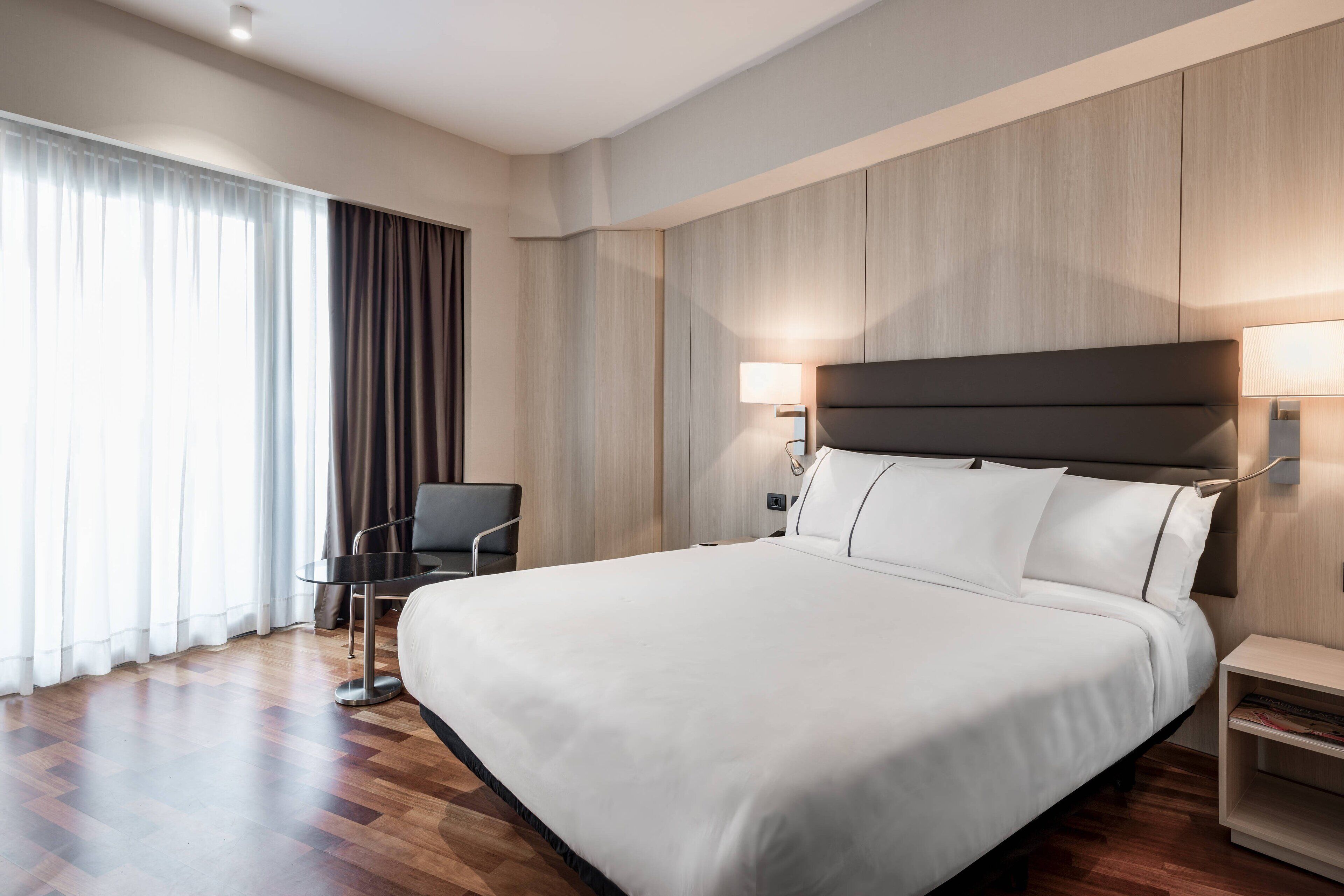 A modern hotel room with a large bed, a desk, and a chair.