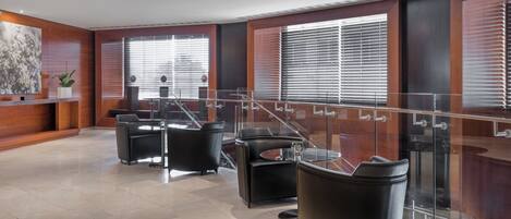 A modern lobby with a glass railing, black leather seating, and a staircase.