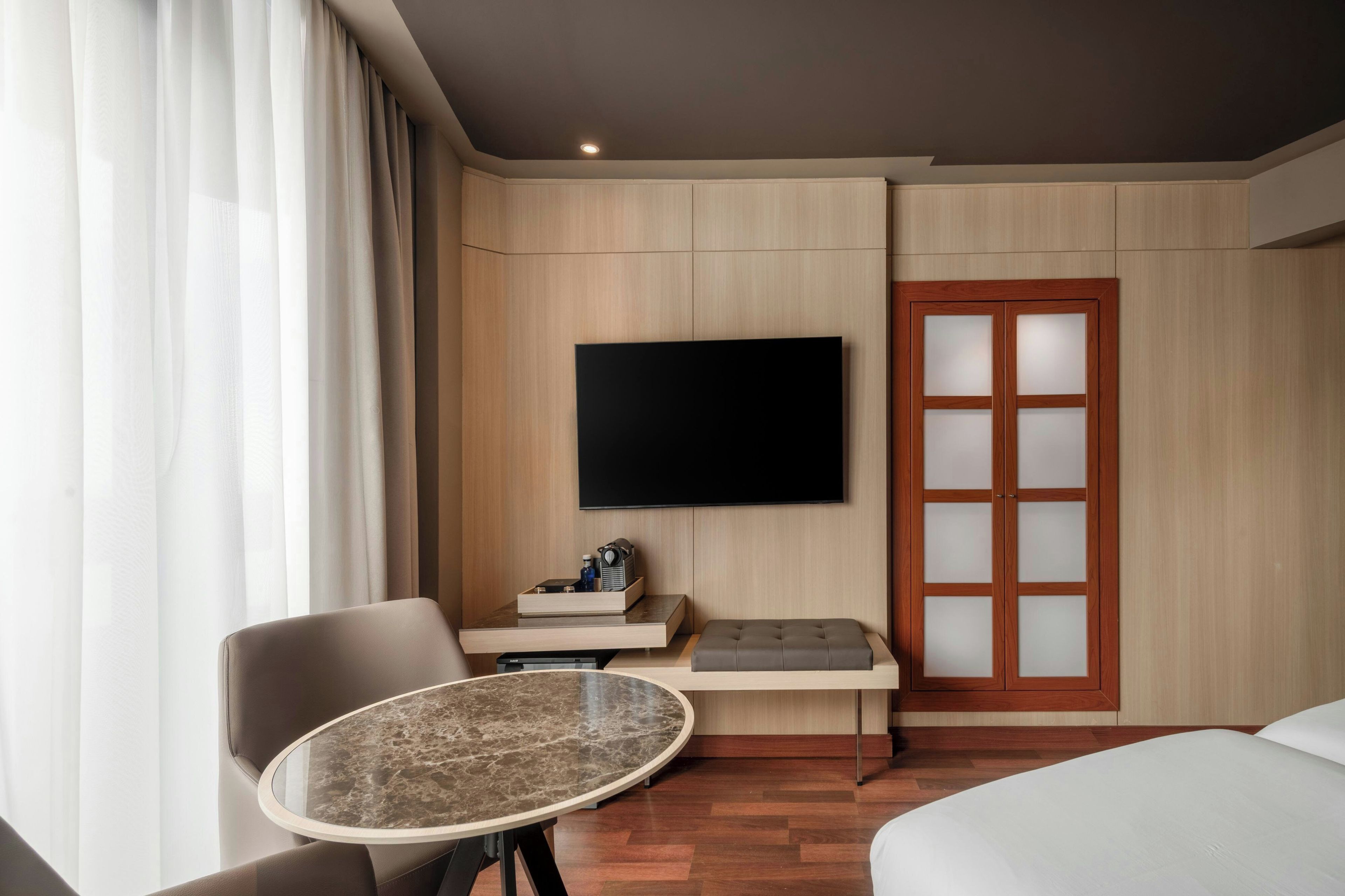 A hotel room with a bed, a TV mounted on the wall, a small table, and a chair.