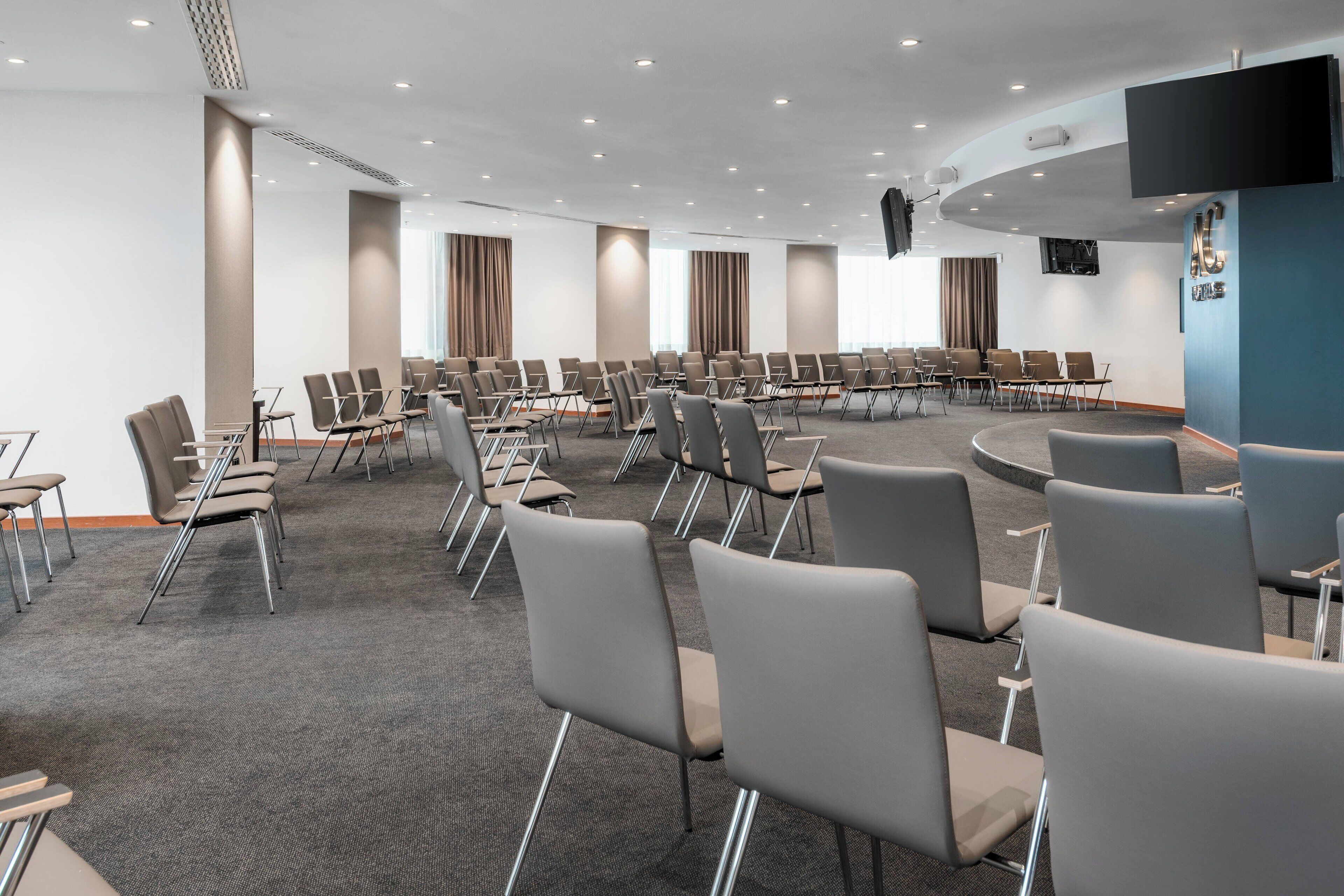 Un salón de conferencias con filas de sillas, una pantalla grande y una pared azul de acento.