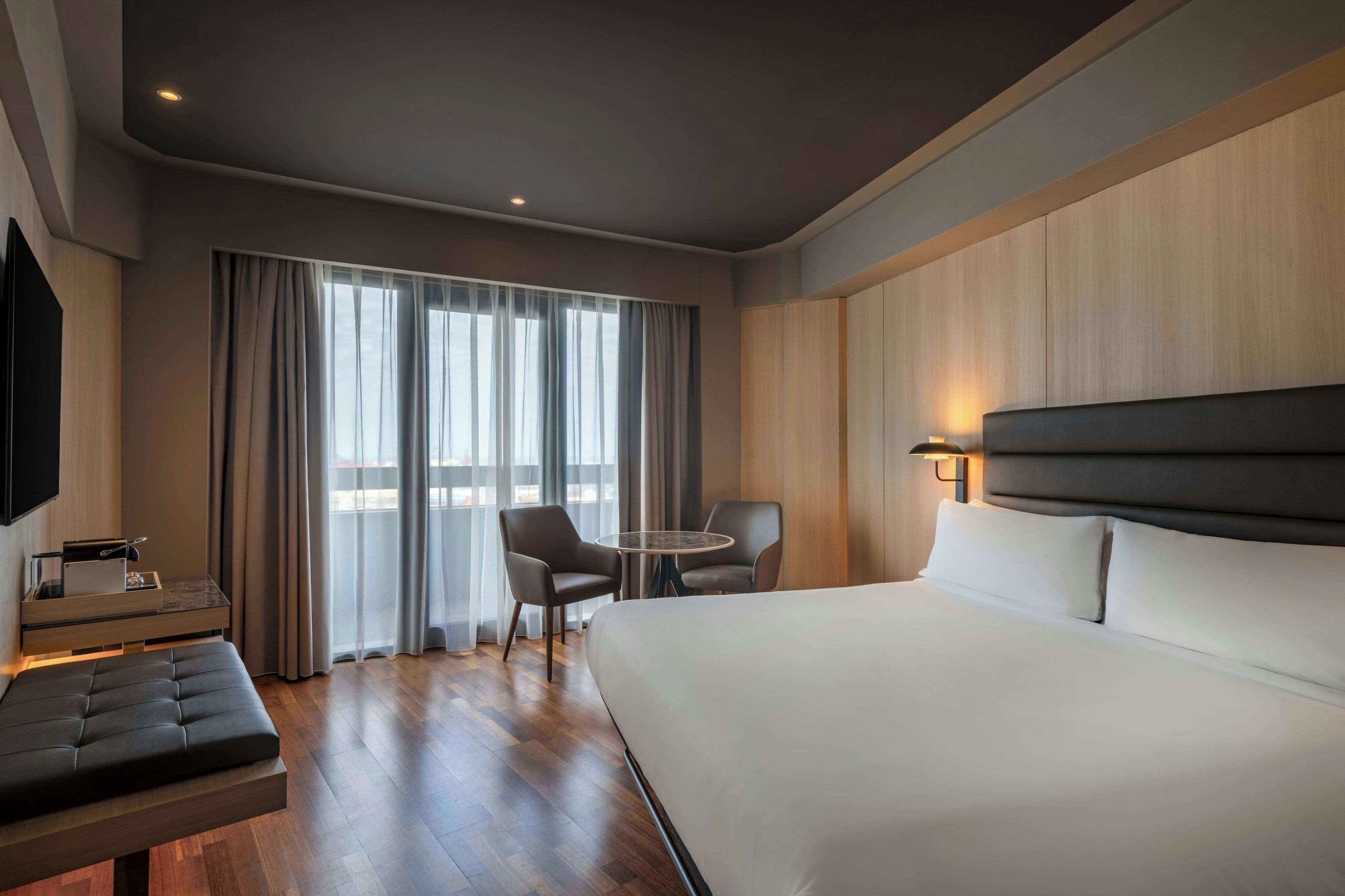 Una camera d'albergo con un letto grande, una scrivania, una sedia, un tavolino rotondo e un televisore.