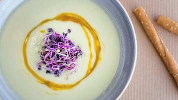 Un tazón de sopa con un hilo de aceite y adornado con brotes morados, acompañado de un pretzel sobre una superficie rugosa.