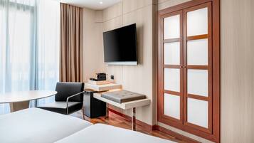Une chambre d’hôtel comprenant un lit, un bureau, une chaise, un téléviseur fixé au mur et une grande fenêtre avec des rideaux.