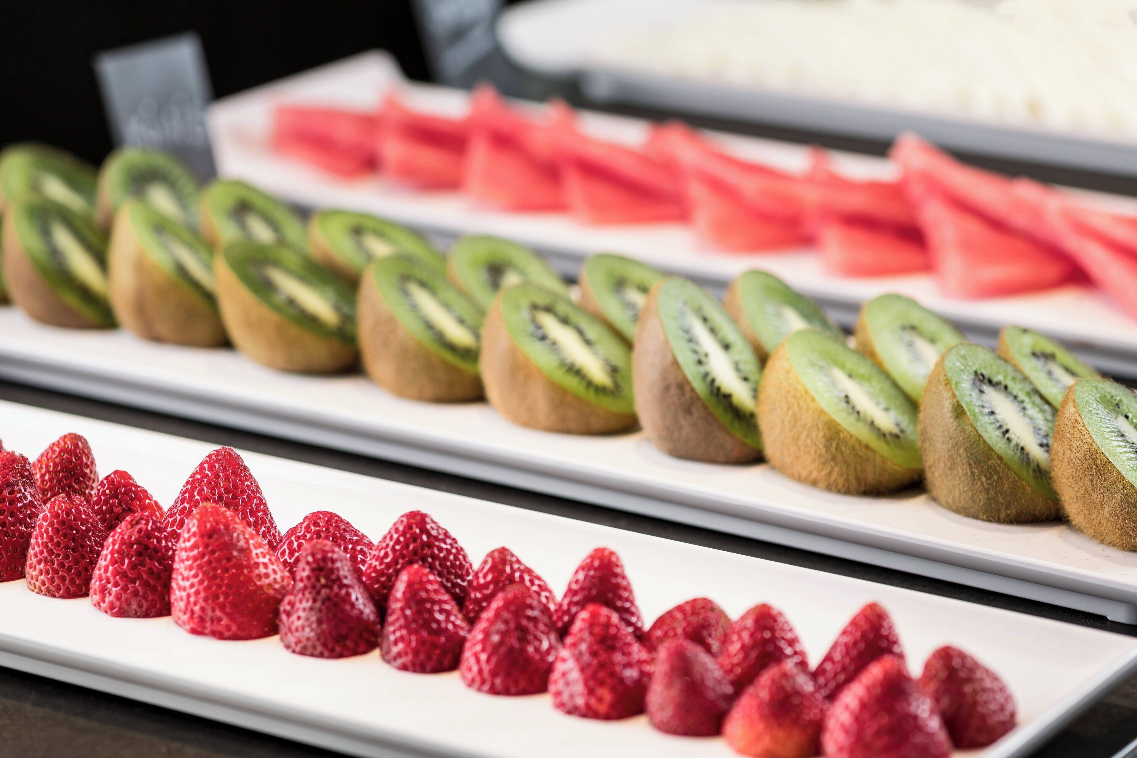Un bufé con frutas cortadas y dispuestas con cuidado, incluyendo fresas, kiwi y sandía.