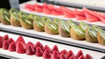 Un bufé con frutas cortadas y dispuestas con cuidado, incluyendo fresas, kiwi y sandía.
