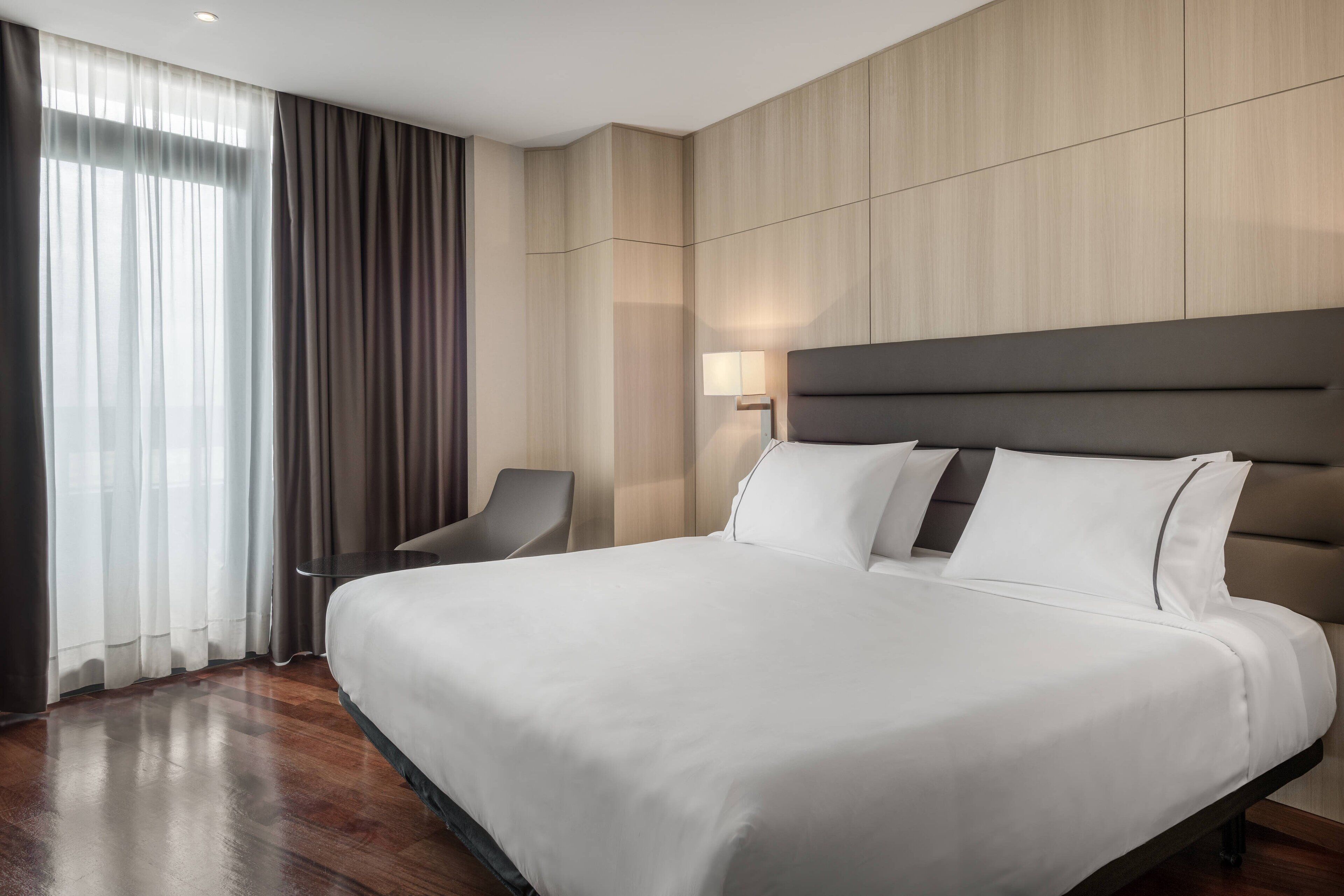A hotel room with a large bed, a chair, a desk, and a lamp.