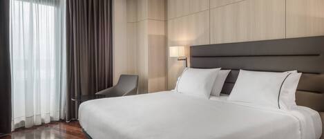 A hotel room with a large bed, a chair, a desk, and a lamp.
