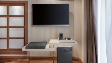 Una habitación moderna con televisión de pantalla plana en la pared, una pequeña mesa con un banco y un refrigerador compacto.