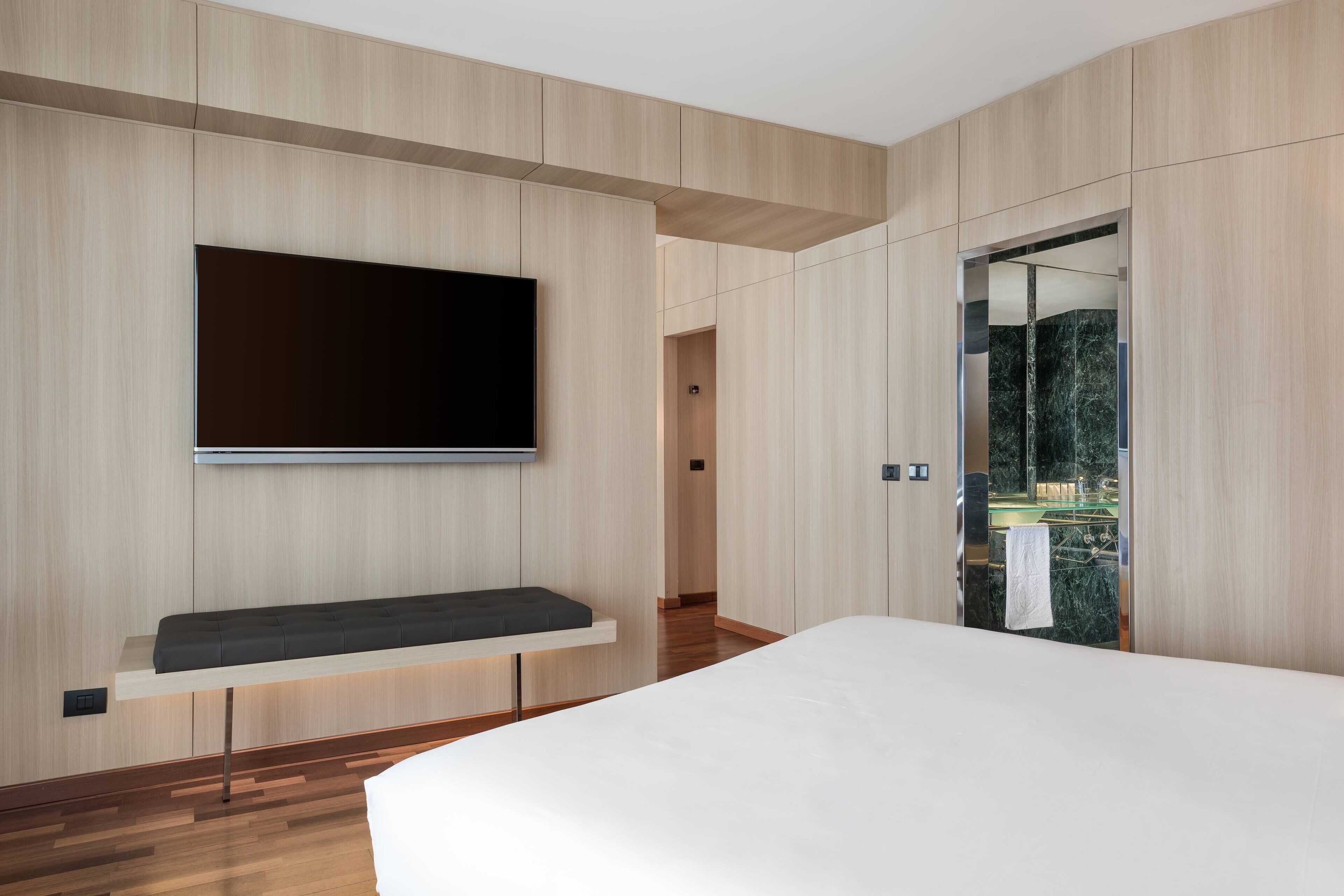 Un dormitorio moderno con una cama grande, un televisor montado y un panel de pared de madera.
