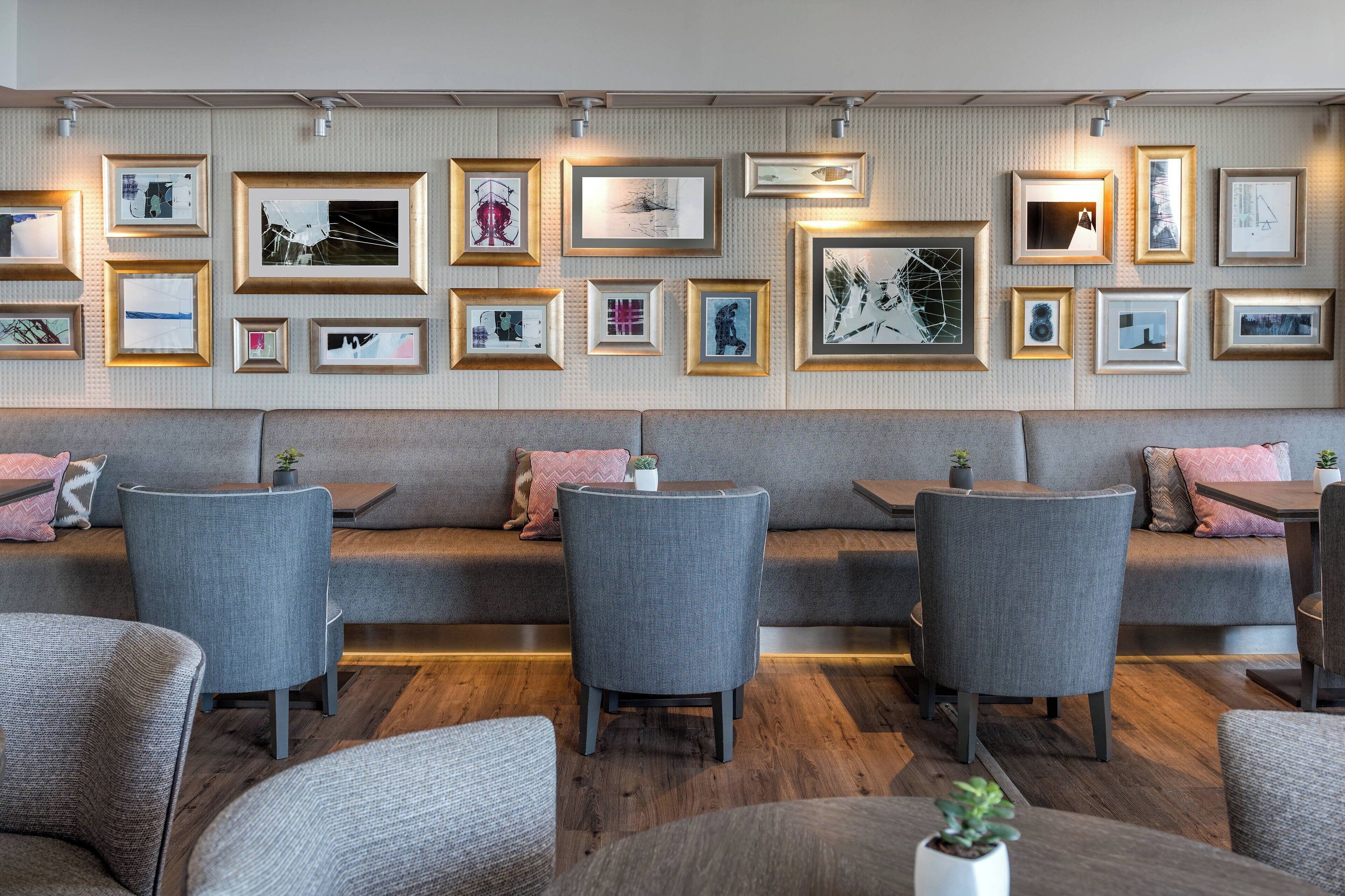 A modern interior with a seating area featuring grey upholstered sofas and chairs, a wall adorned with framed artworks, and a wooden floor.