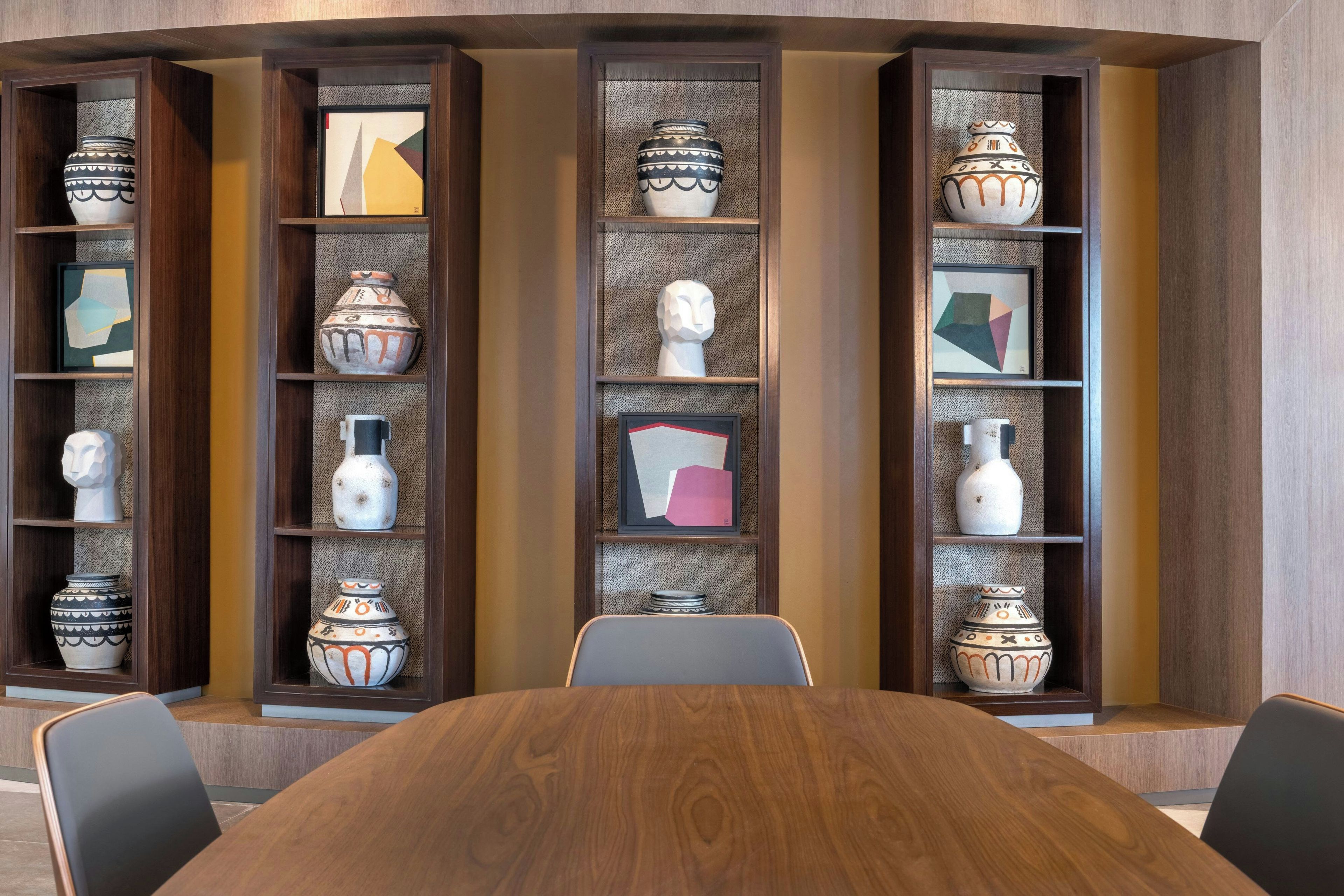 A conference room with a wooden table and chairs, surrounded by shelves with decorative vases and framed artwork.