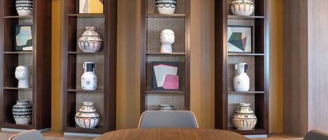 A conference room with a wooden table and chairs, surrounded by shelves with decorative vases and framed artwork.