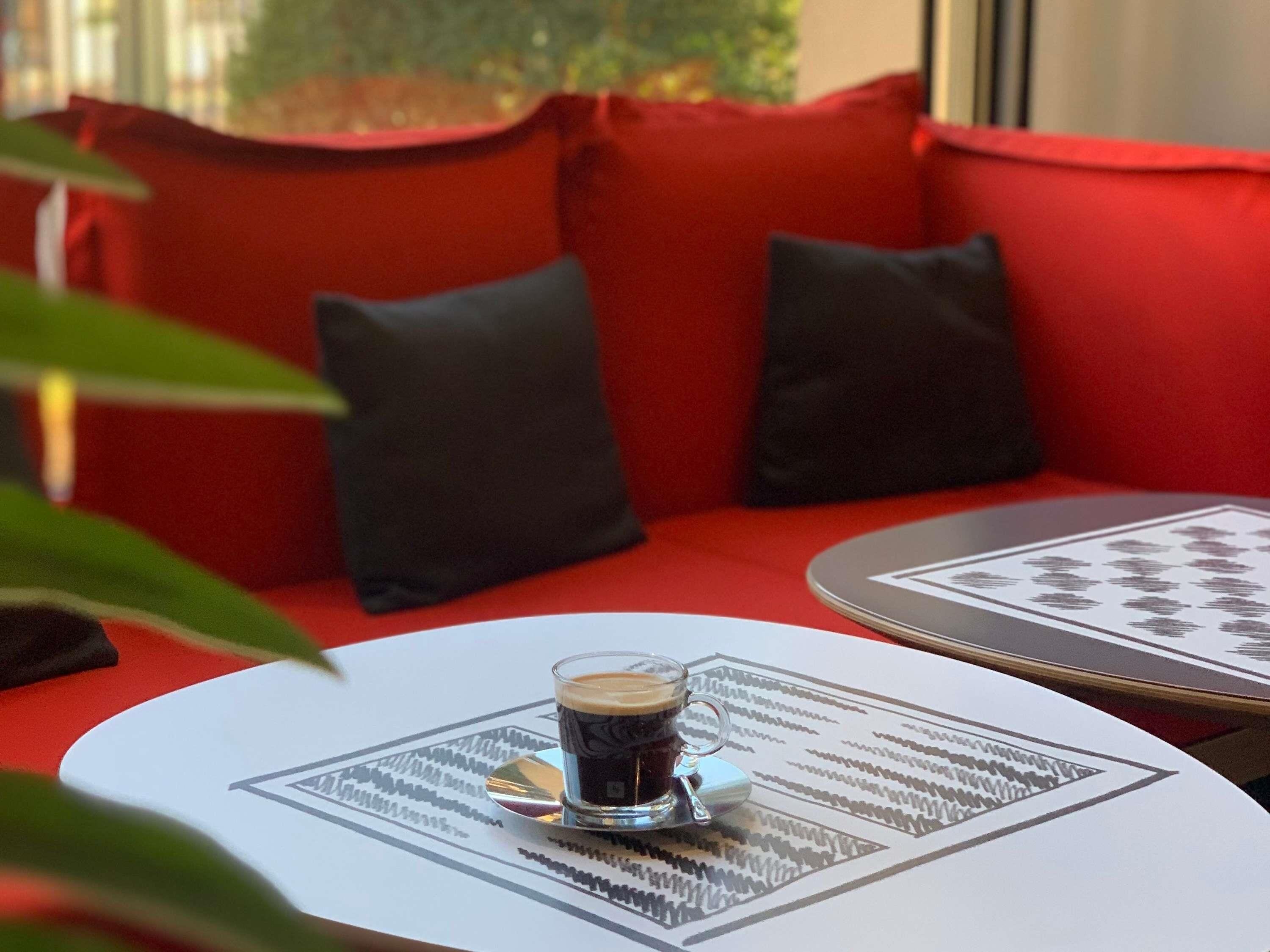 A seating area with red cushions, a glass of coffee on a coaster, and a patterned table mat.