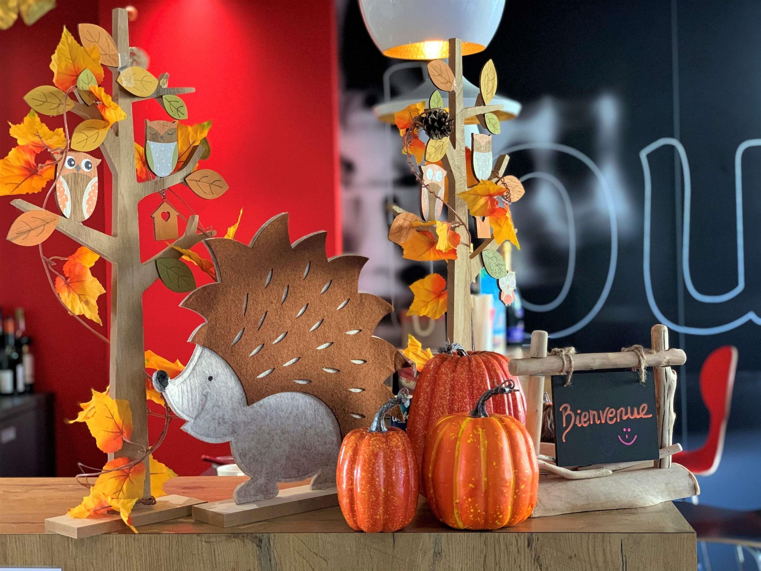 Ein Holztisch mit einer dekorativen Herbstdekoration, darunter ein Baum, eine Eule, ein Igel und Kürbisse.