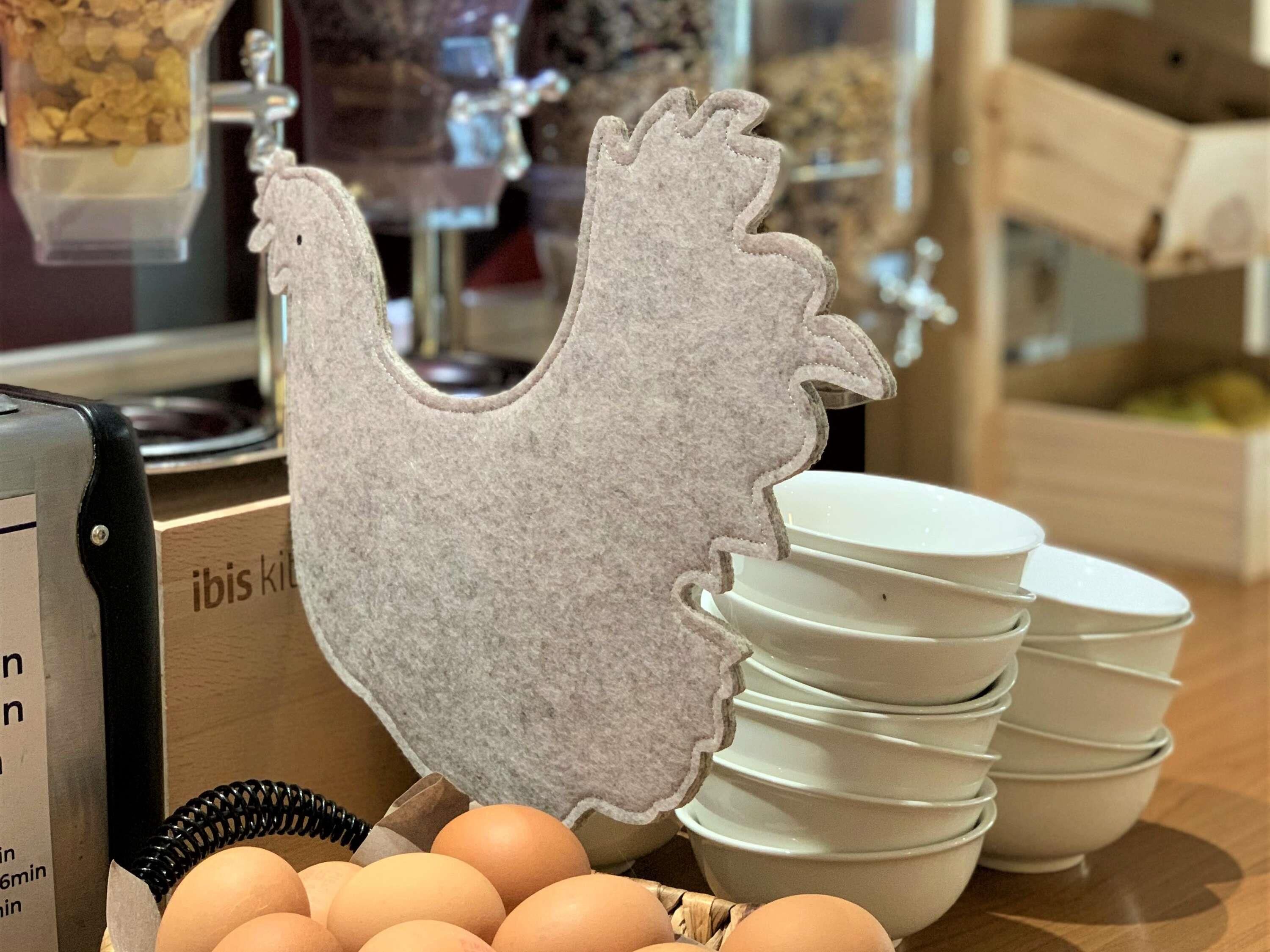A kitchen counter with a stack of white bowls, a basket of eggs, and a felt chicken decoration.