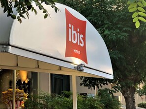 A sign for ibis hotels with a modern design, located in an urban setting with visible greenery and a building facade in the background. - ibis Cannes Plage La Bocca (Cannes)