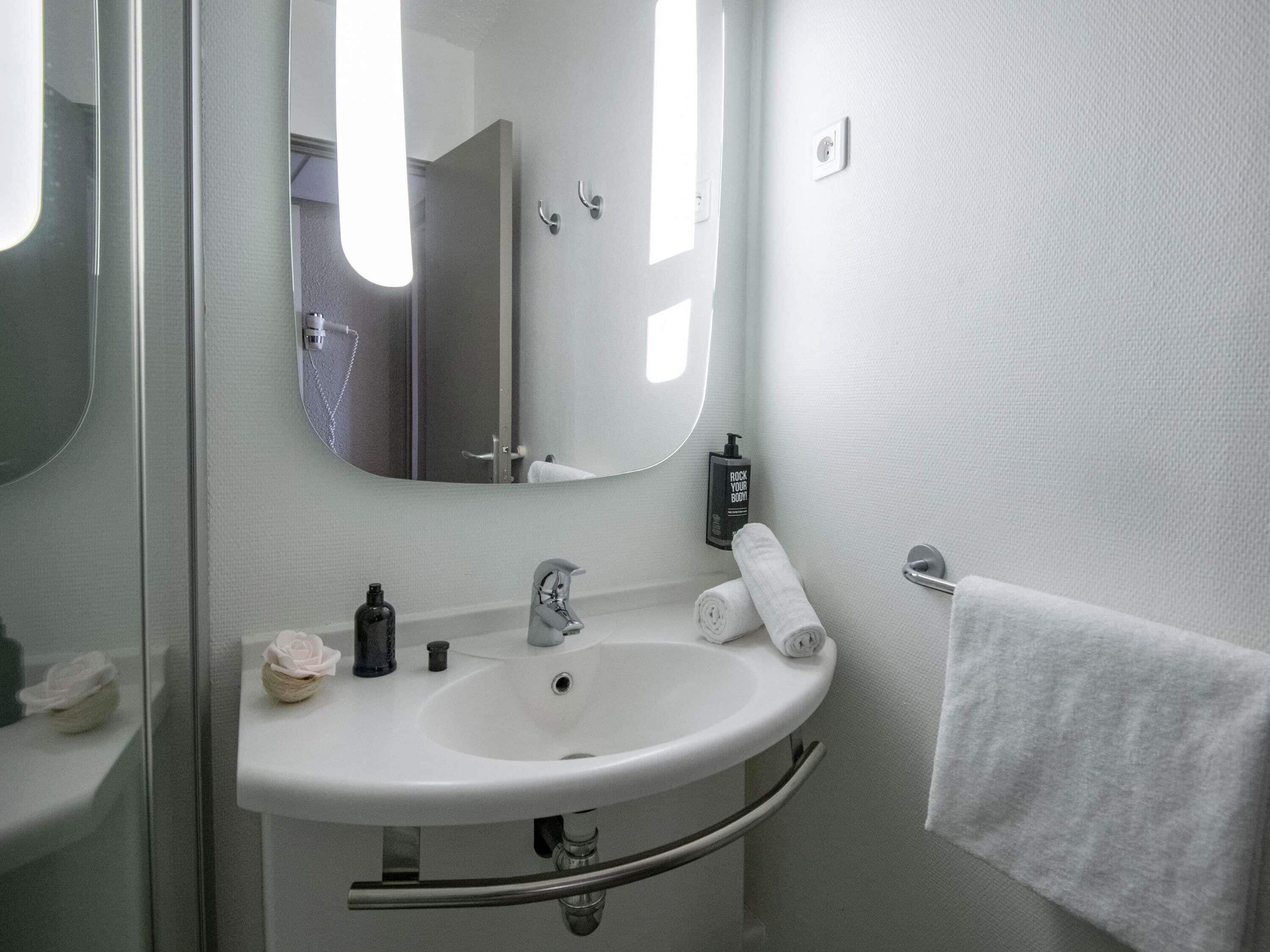 Un baño con un lavabo blanco, un espejo, una toalla y una botella de loción.