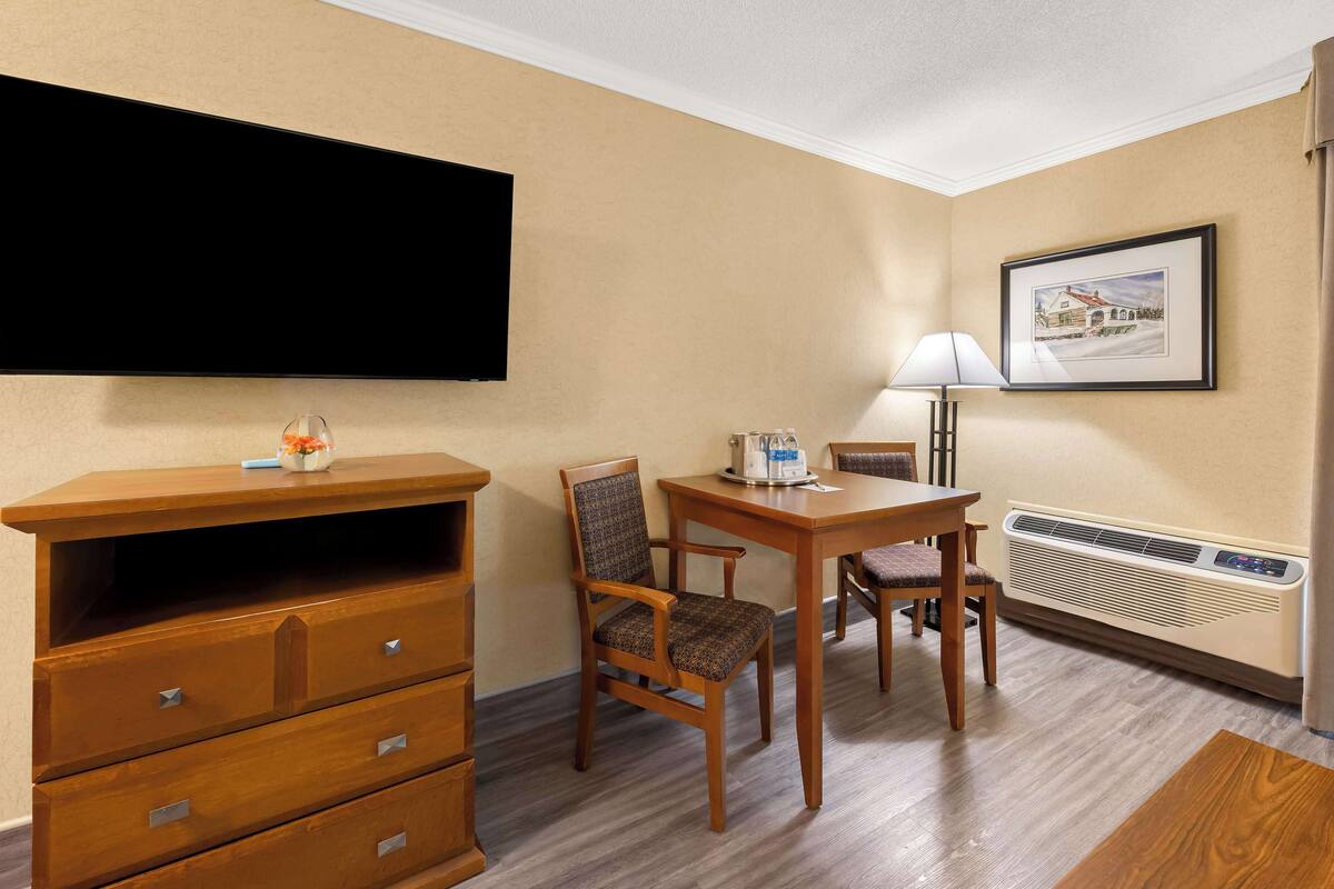 Habitación de hotel con televisión de pantalla plana, cómoda de madera, dos sillas, una mesa, una lámpara y un cuadro en la pared.