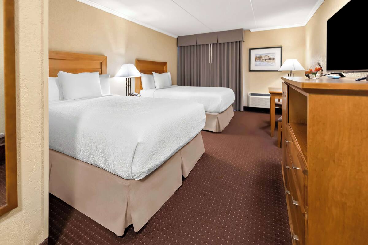 Habitación de hotel con dos camas, un escritorio, una silla, una lámpara y un cuadro en la pared.