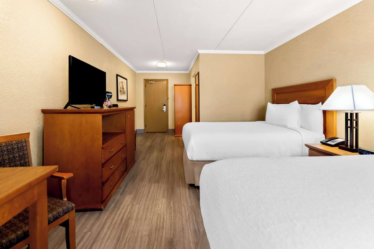 Habitación de hotel con dos camas, un escritorio, un televisor y una lámpara.