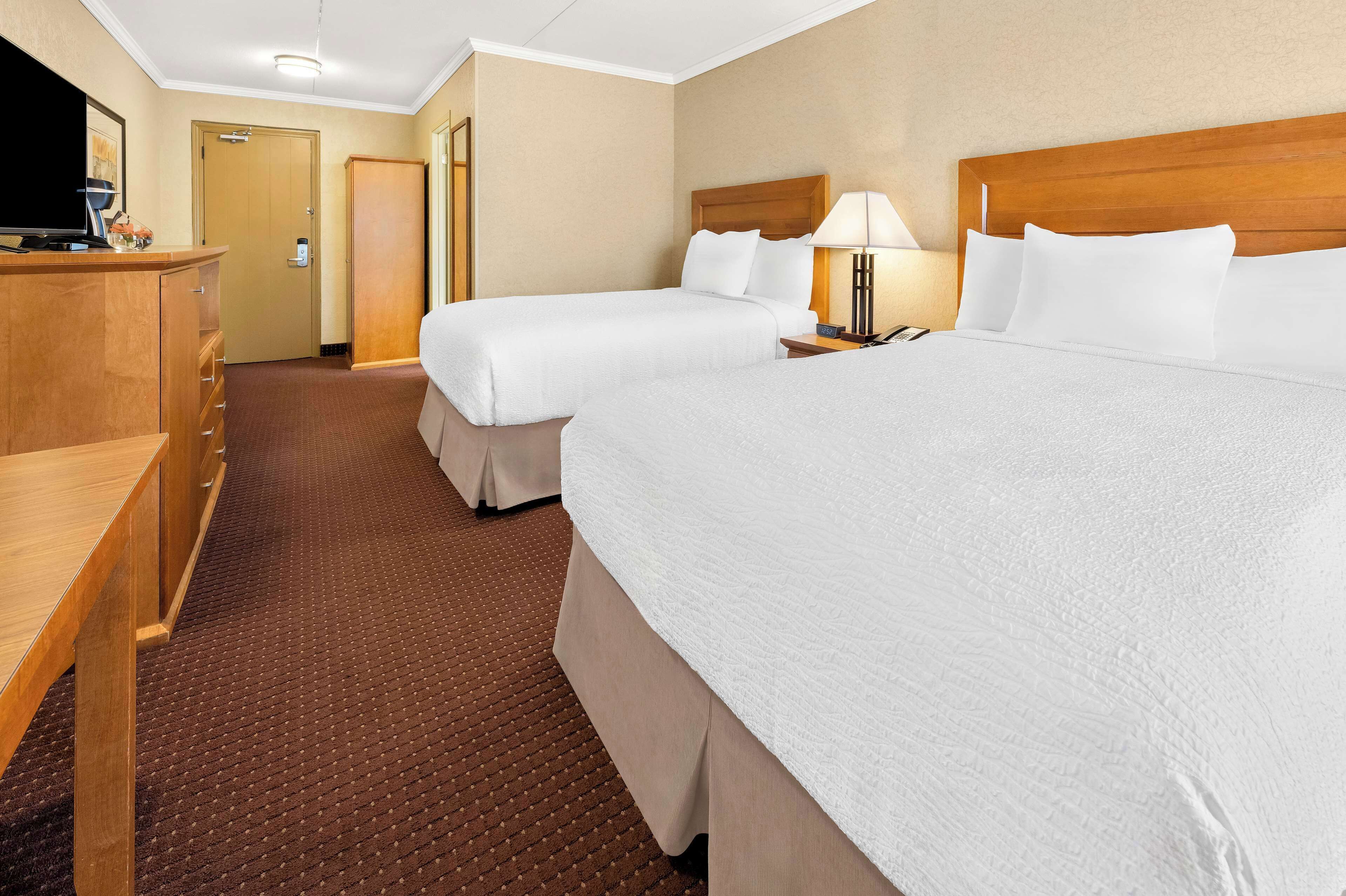 A hotel room with two beds, a wooden desk, a TV, and a lamp.
