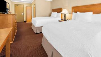 A hotel room with two beds, a wooden desk, a TV, and a lamp.