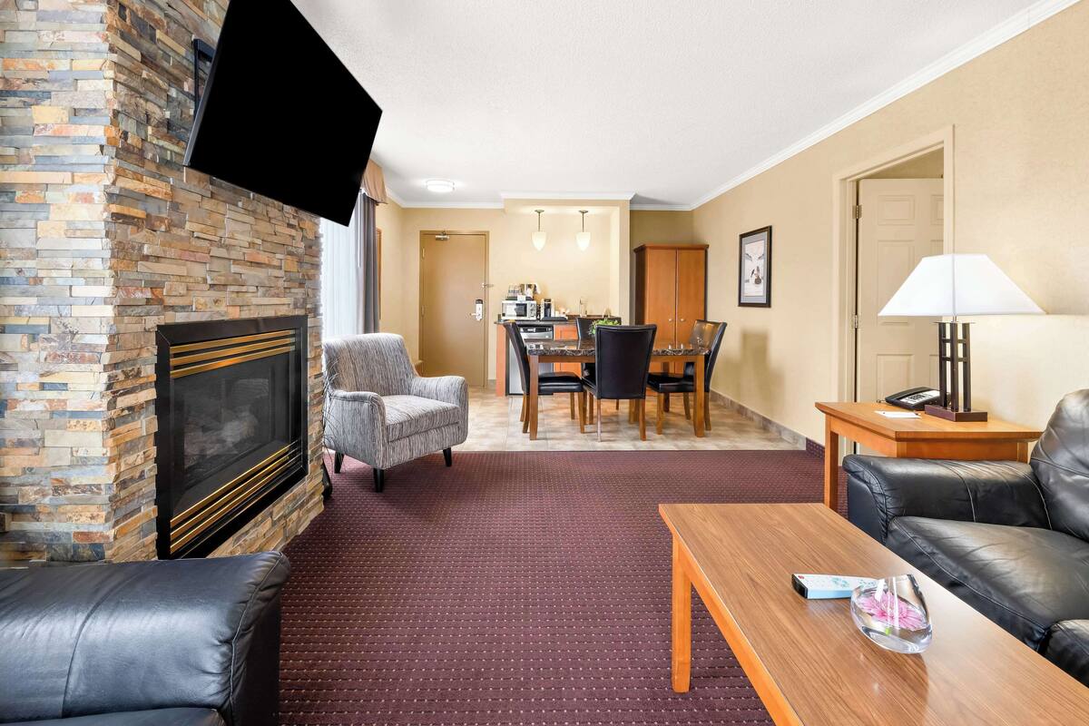 Una sala de estar con chimenea, sofás de cuero, un comedor con mesa y sillas, y un televisor montado en la pared.