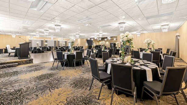 A large banquet hall with tables set for dining, chandeliers, and a carpeted floor.