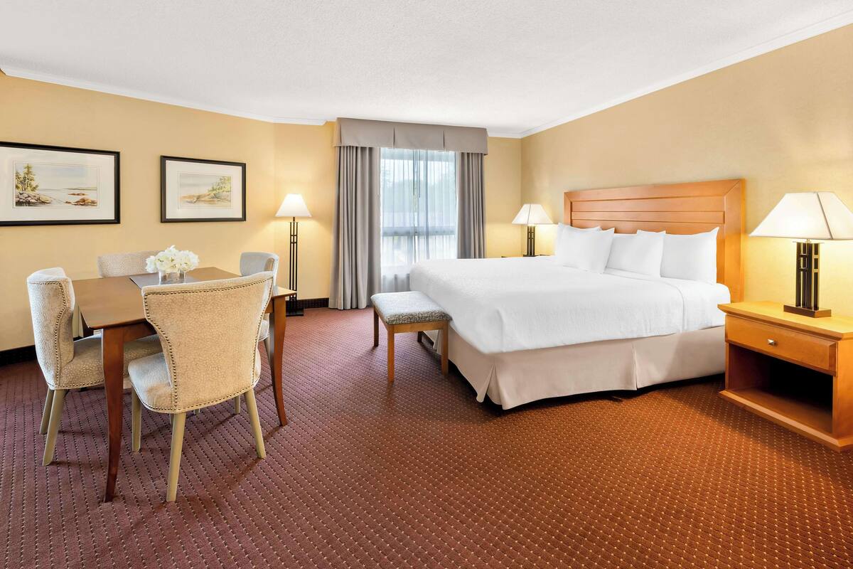 Habitación de hotel con cama, mesita de noche, lámpara, escritorio con silla y dos cuadros en la pared.
