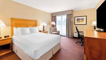 A hotel room with a large bed, two bedside tables with lamps, a desk with a chair, a television, and a framed picture on the wall.