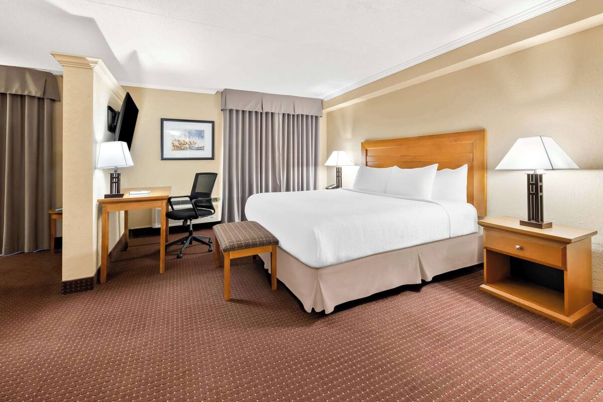 Habitación de hotel con una cama grande, dos mesitas de noche con lámparas, un escritorio con silla y un ventanal con cortinas.