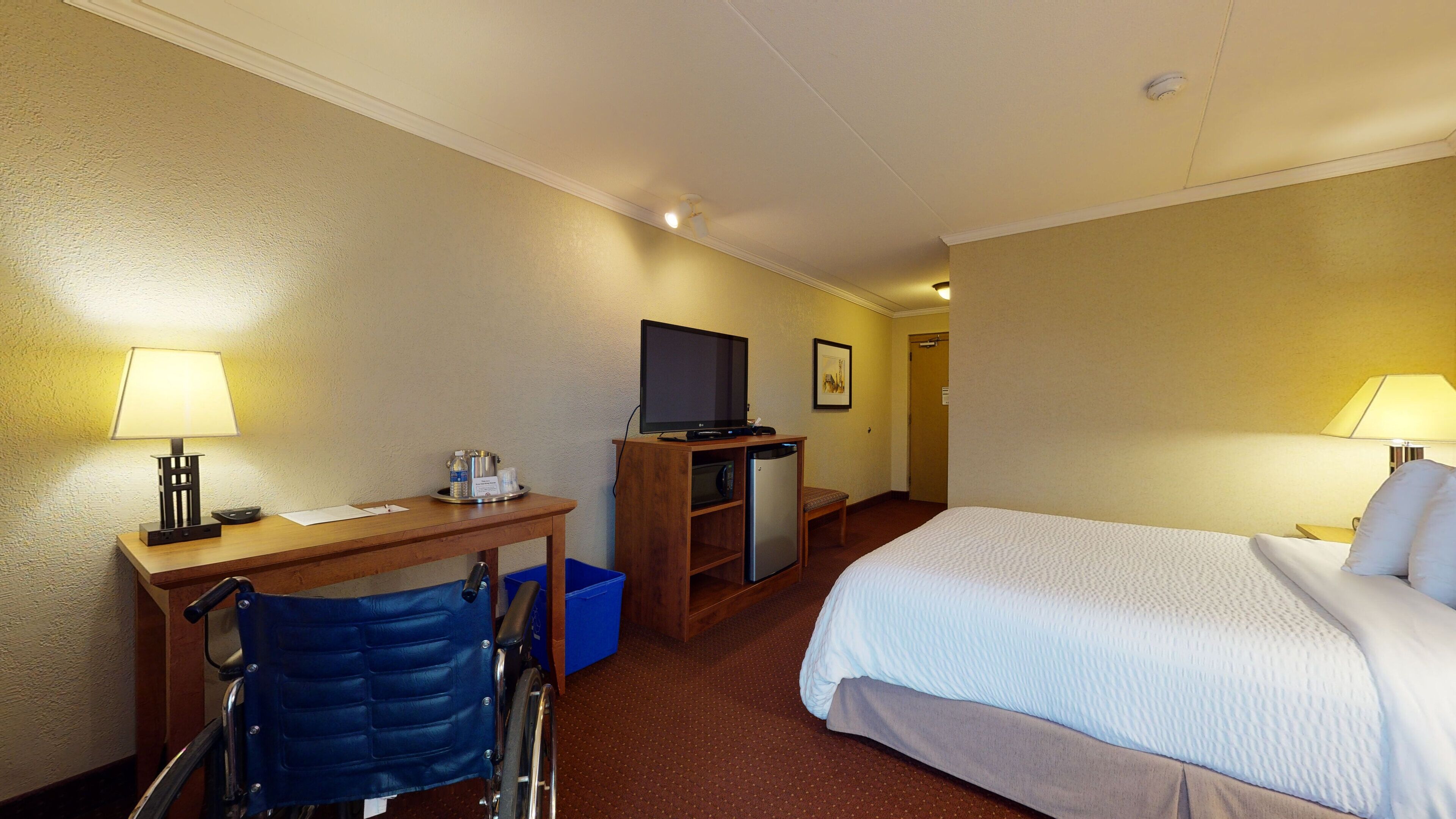 A hotel room with a bed, desk, chair, television, and a small refrigerator.