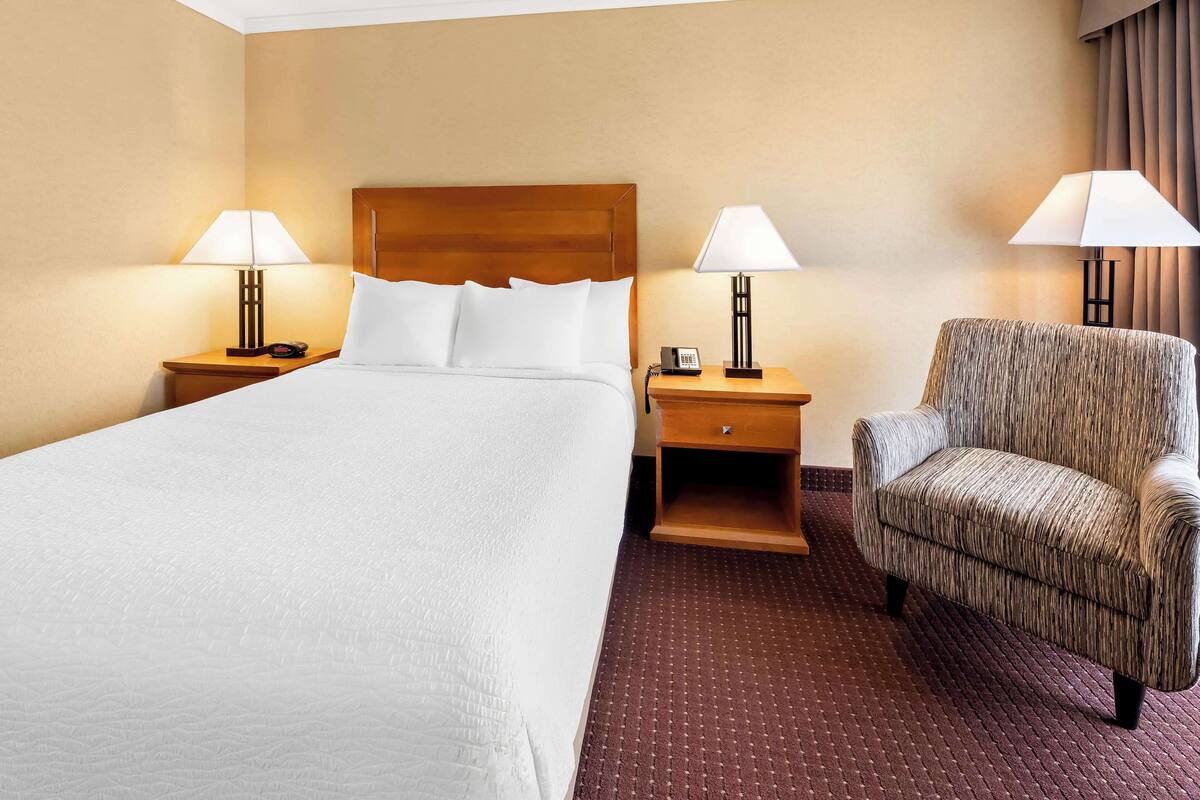 Una habitación de hotel con una cama grande, dos mesitas de noche con lámparas, una silla y un pequeño tocador de madera.