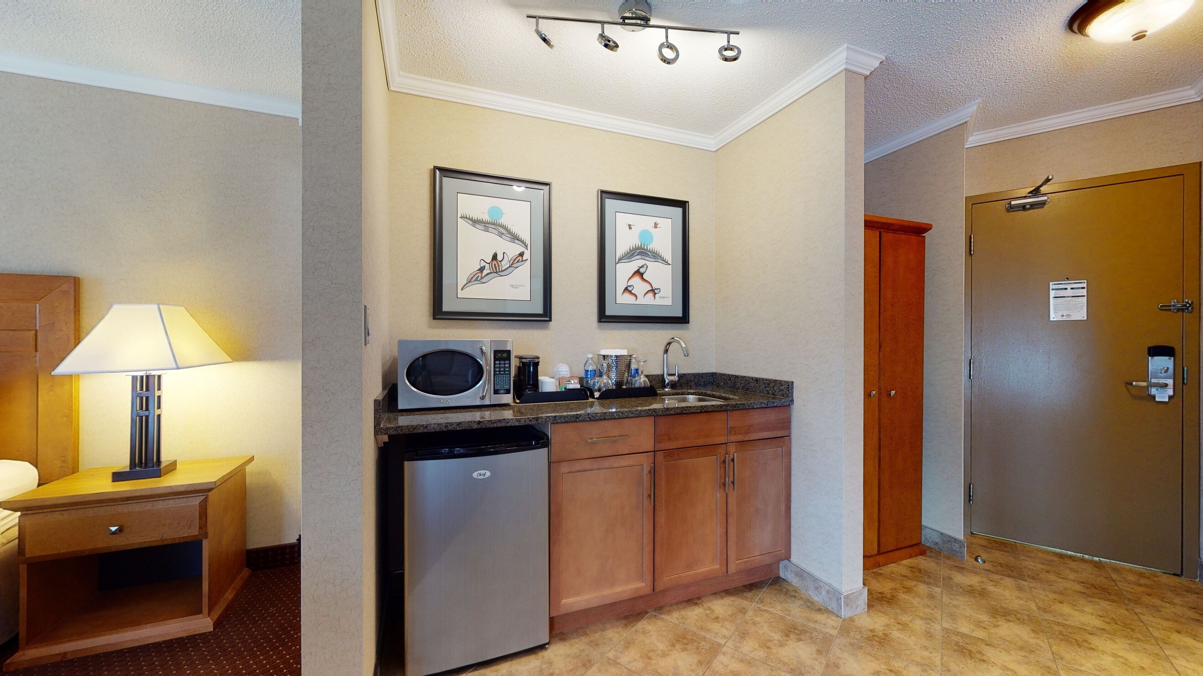 A compact kitchen with a microwave, coffee maker, and a sink. There are framed pictures on the wall and a wooden cabinet.