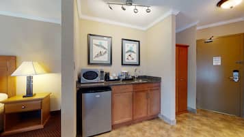 A compact kitchen with a microwave, coffee maker, and a sink. There are framed pictures on the wall and a wooden cabinet.