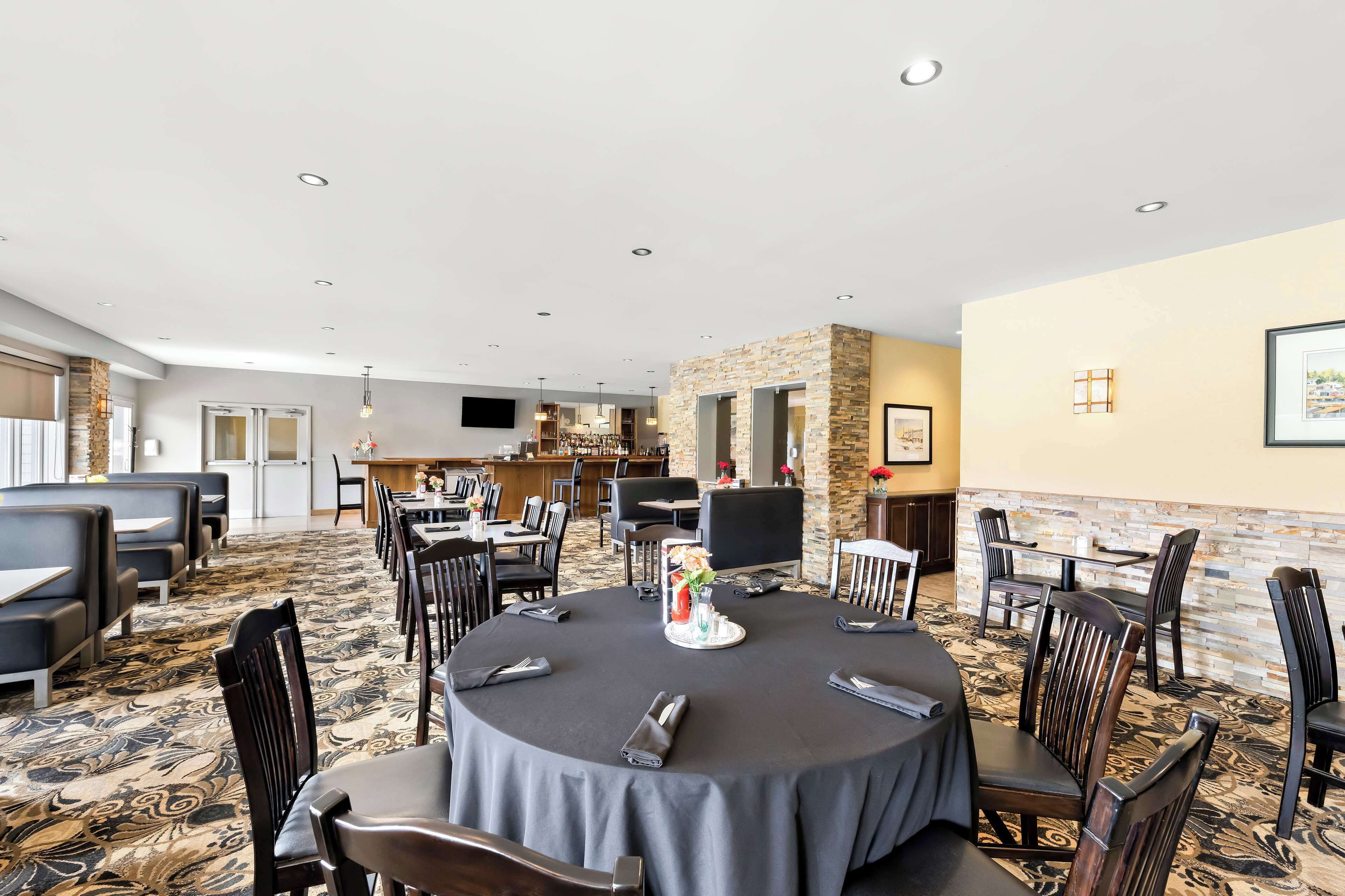 A hotel dining area with round tables, black chairs, and a patterned carpet.