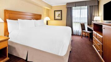 A hotel room with a large bed, a desk, a chair, a TV, and a dresser.