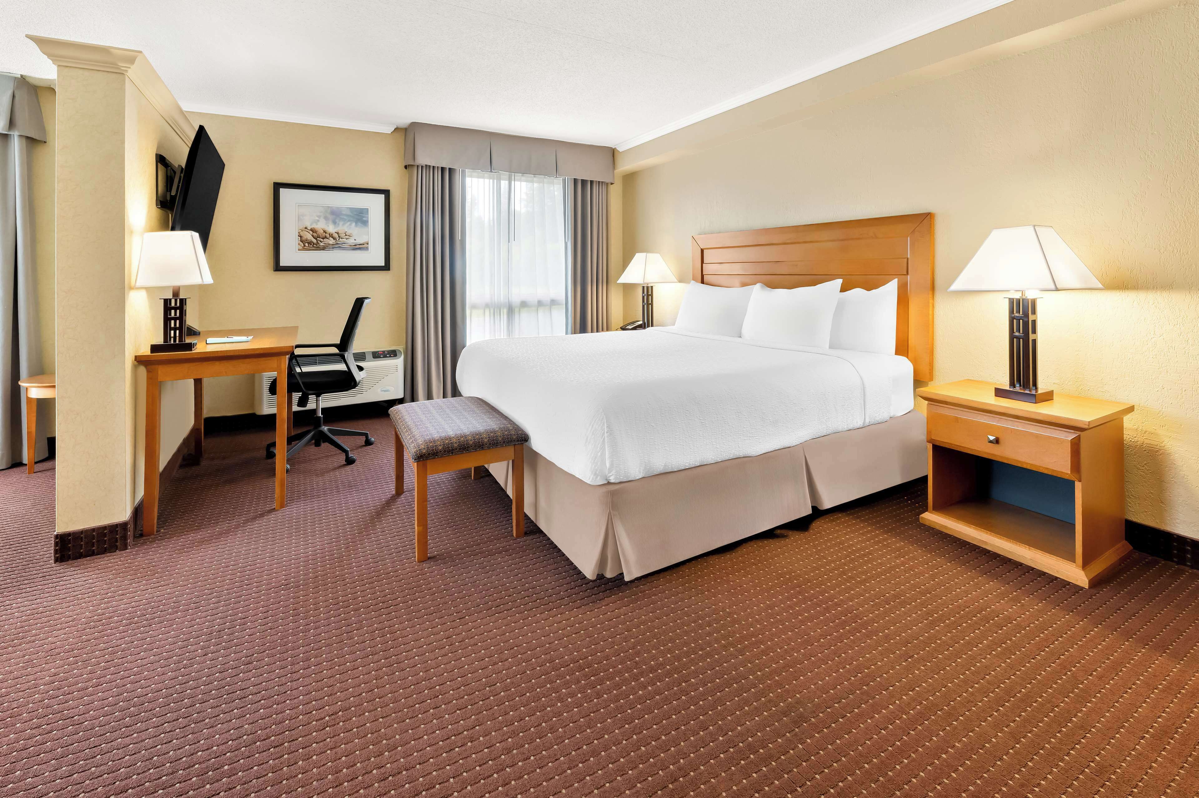 Une chambre d’hôtel avec un grand lit, deux tables de chevet avec des lampes, un bureau avec une chaise et un téléviseur fixé au mur.