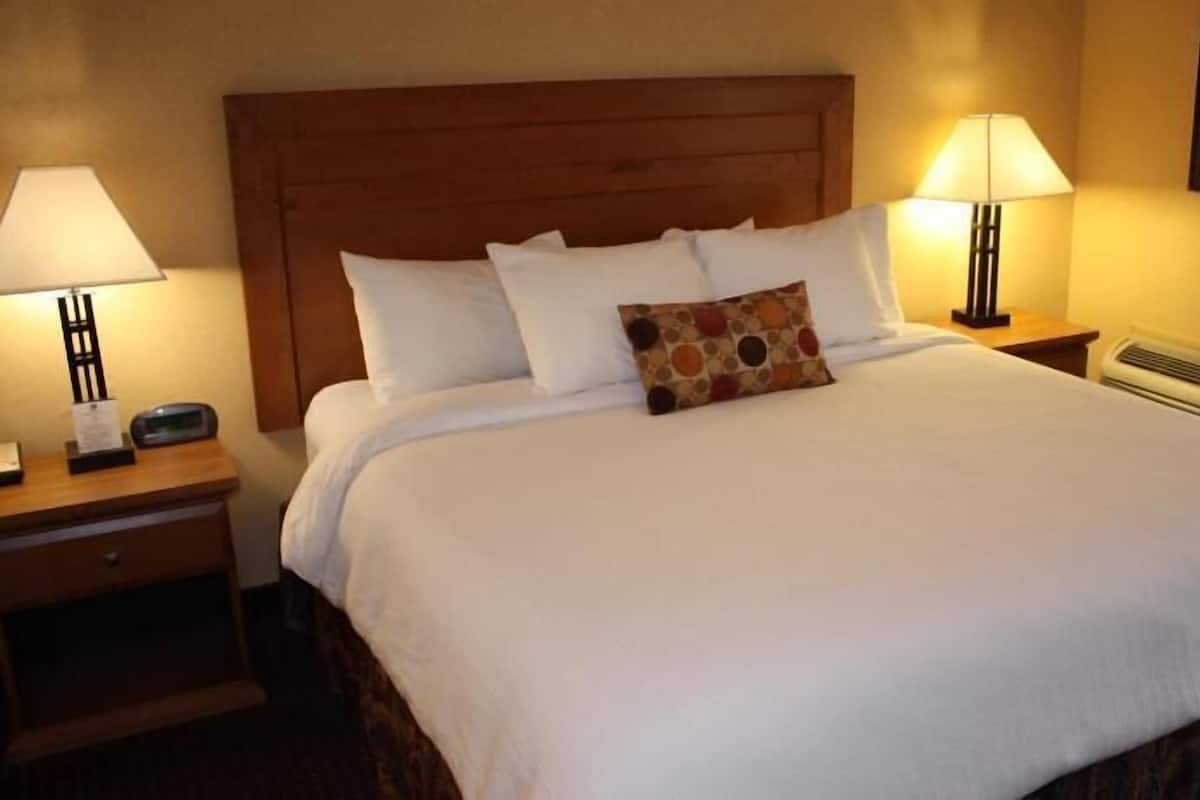 Habitación de hotel con cabecera de madera, ropa de cama blanca, dos lámparas de noche, una mesita de noche y aire acondicionado instalado en la pared.