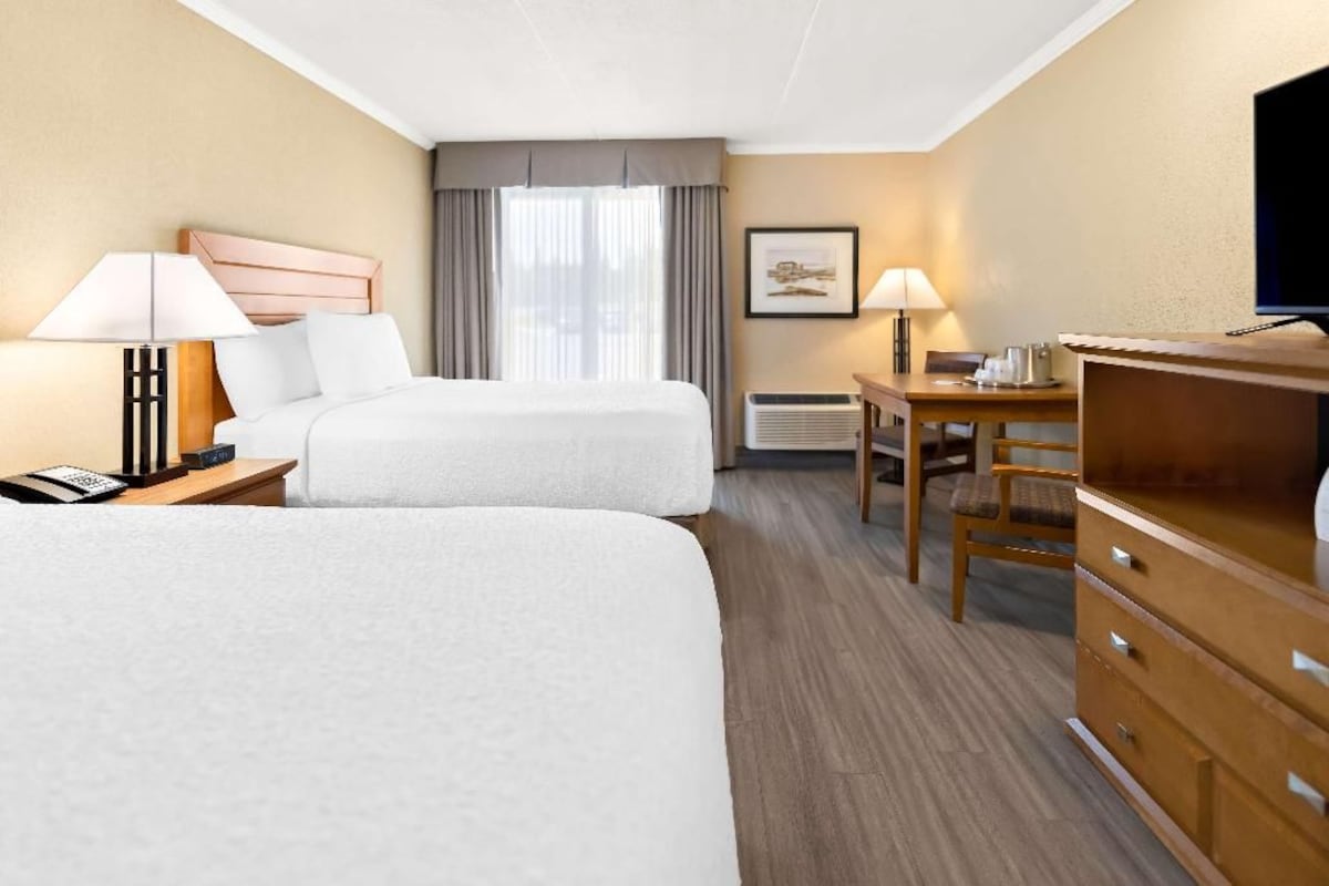 A hotel room with two beds, a desk, a chair, a television, and a framed picture on the wall.