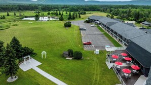 A hotel with a parking lot, outdoor seating area with umbrellas, and a view of a lake and forested hills. - Best Western Plus Nor'wester Hotel & Conference Centre (Thunder Bay)