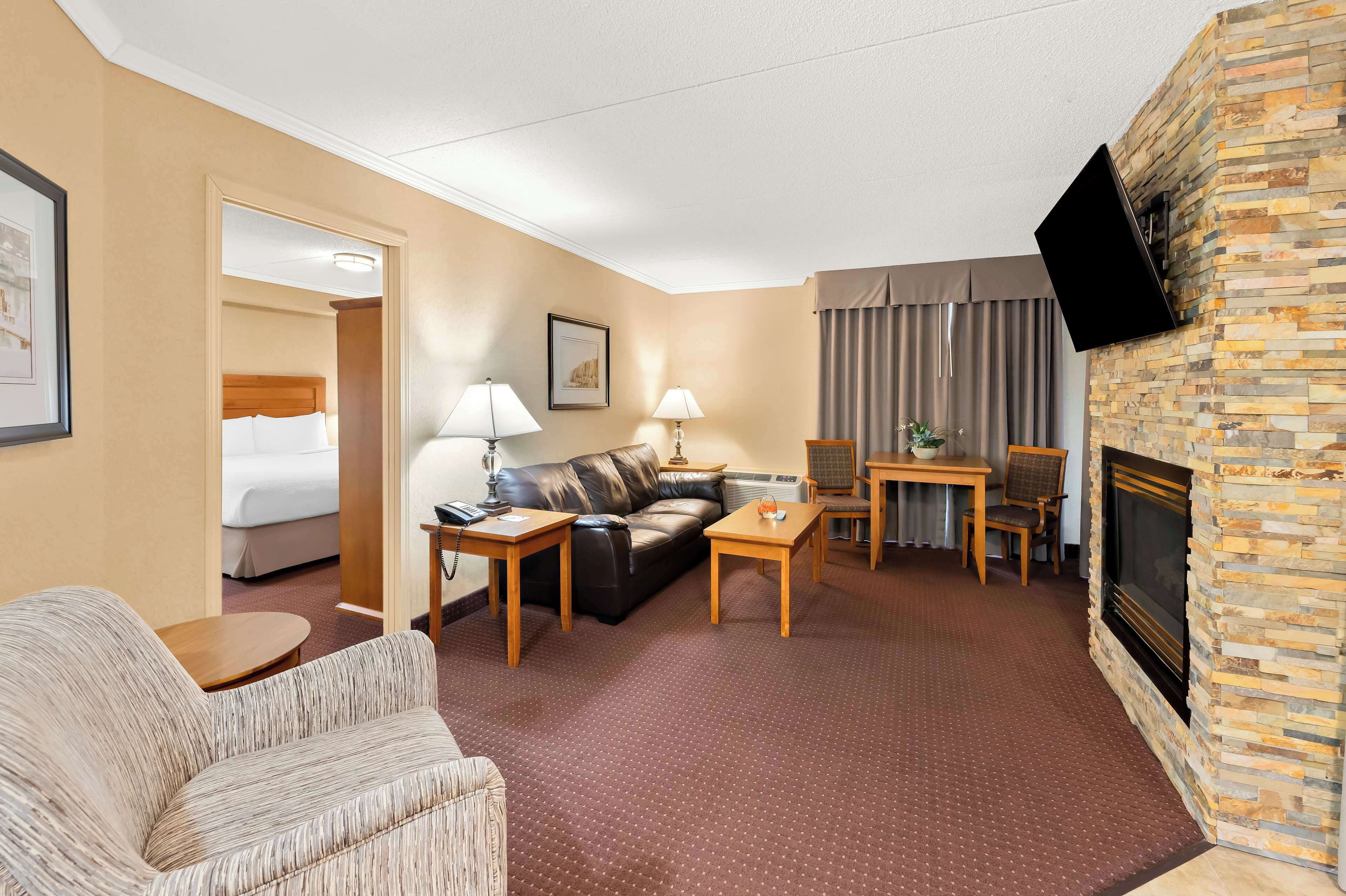 Una habitación de hotel con una cama, un sofá de cuero, una mesa de centro, un televisor instalado en la pared y una chimenea.