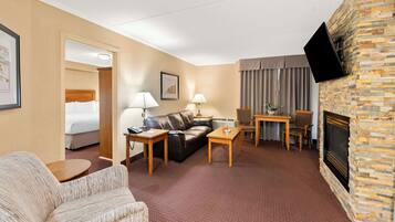 Una habitación de hotel con una cama, un sofá de cuero, una mesa de centro, un televisor instalado en la pared y una chimenea.